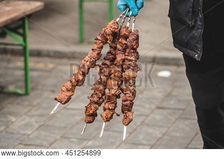 Man Holding Pork Meat Skewers, Grilled Or Roasted In A Barbecue On An Open Fire And Flames, Shashlik