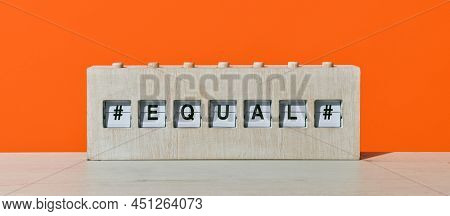 the word equal in a rustic wooden split flap board, on a wooden surface against an orange background, in a panoramic format to use as web banner or header