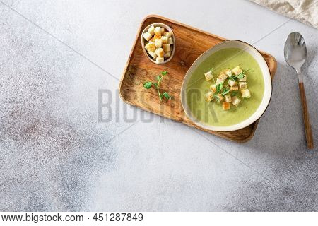Green Vegetable Cream Soup In A White Bowl On A Gray Concrete Background Top View. Vegan Soup Puree