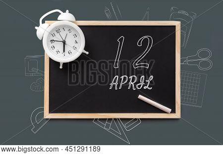 April 12. 12th Day Of Month, Calendar Date.   Blackboard With Piece Of Chalk And White Alarm Clock O