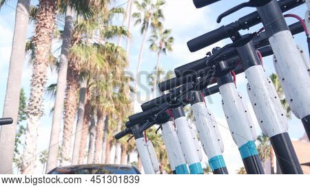 Row Of Rental Electric Scooters Parked On Street Sidewalk, Many Palm Trees In City Near Los Angeles,