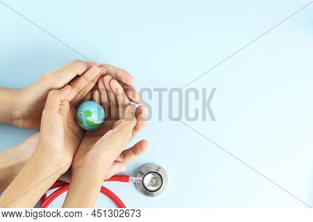 World Health Day Concept - Hands Hold Blue Earth On Blue Background With Stethoscope