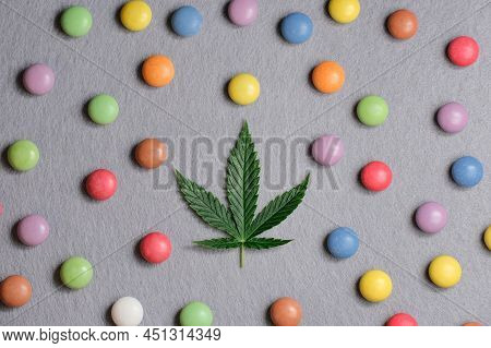 Cannabis Leaf With Colorful Candy Confetti Close Up. Marijuana Sweets With Cbd And Thc On Gray 
Back