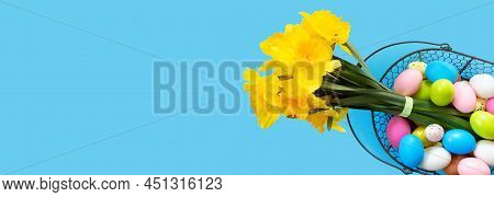 Basket With Easter Eggs And Bouquet Of Yellow Narcissus On Blue Paper Background. Flat Lay  Top View