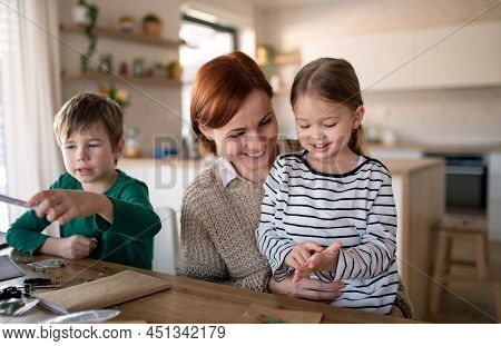 Mother Of Little Children Supervising Them When Diong Homework At Home.