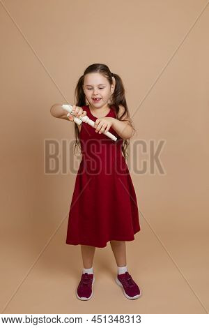 Girl In Red Dress Enthusiastically Disassemble Common Flute In Parts, Beige Background. Learning To 