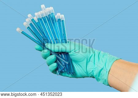 Dentist's Hand In A Latex Glove With Saliva Ejectors On The Blue Background. Medical Tools Concept.