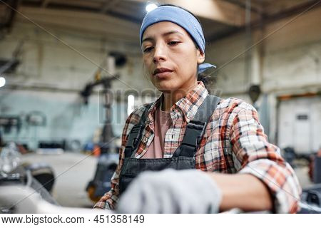 Young Hispanic workwoman or repairperson in coveralls, blue headband and gloves choosing handtools for repairing machines
