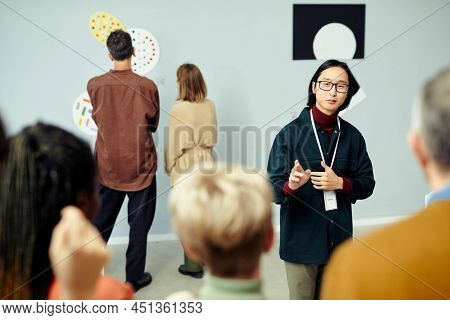 Young Asian Gallerist Standing In Front Of Group Of Tourists Speaking About Contemporary Artworks De