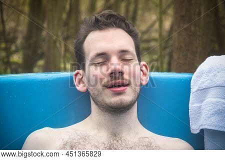 Man Relaxing In An Outdoor Bath Surrounded By Trees, Around Camping Site In Gloucestershire, England