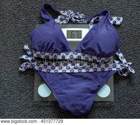 Bikini On A Glass Scale Which Marks 67 Kg, Dark Gray Carpet In Background