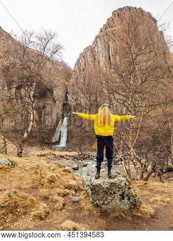 A Woman With Her Face Hidden Under Her Hair Stands On A Rock In A Rocky Gorge With A Waterfall In Th