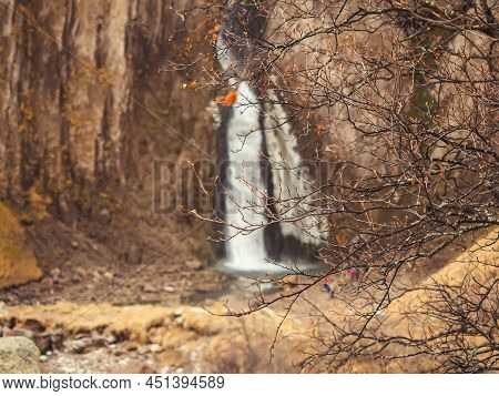Bare Branches Of An Autumn Tree Against The Backdrop Of A Powerful Waterfall Flowing Down From Massi