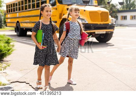 Cheerful Little Girls Next To School Bus. Backback. Back To School Concept.