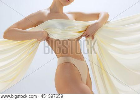 Cropped Female Body In Light Underwear Covered With Milky Colored Silk Fabrik Isolated Over Gray Stu