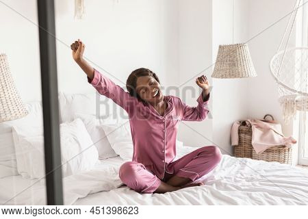 Wellslept African Female Yawning Stretching Arms Sitting In Modern Bedroom