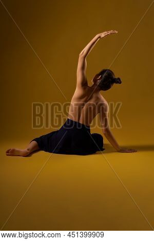 Back View Of Slim Girl Stretching, Bending On Floor. Flexible Young Woman With Hair Bun Sitting Back