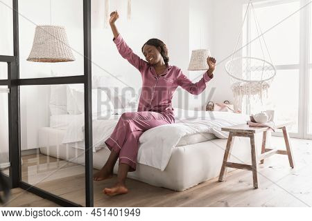 Wellslept Black Lady Stretching Arms Wearing Pajamas Sitting In Bedroom