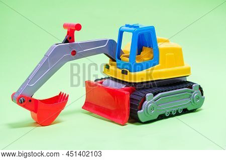 Yellow Excavator Plastic Car On Green Background. Construction Machinery Car For Digging For Toy Sto