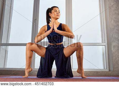 Side View Of Flexible Female Exercising Yoga Pose In Palazzo Pants Indoors. Brunette Woman Sitting W