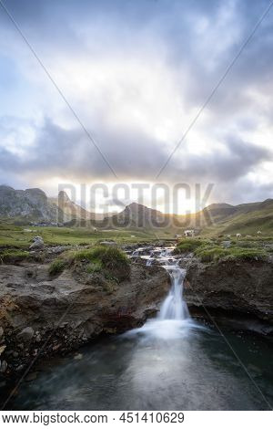 A Meadow On Top Of A Mountain, Surrounded By Rocky Peaks, With A Small River Ending In A Small Water