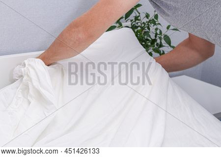 A Man Puts An Elasticated Sheet On The Mattress. Change Of Bed Linen.