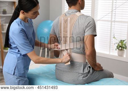 Orthopedist Helping Patient To Put On Posture Corrector In Clinic. Scoliosis Treatment