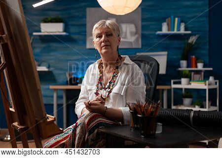 Senior Woman Artist Looking Uninspired Sitting In Front Of Easel Holding Pencil In Home Art Studio. 
