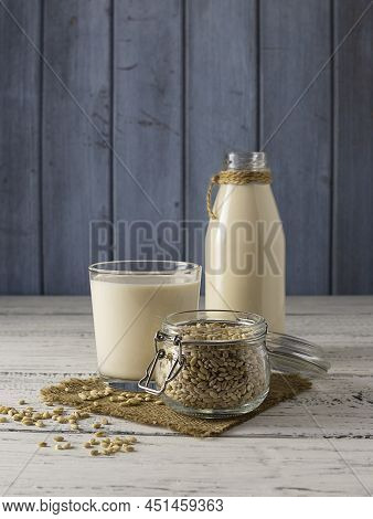 Barley Grains In A Glass Jar On A Canvas Napkin. A Clear Bottle Of Barley Milk And A Glass In The Ba