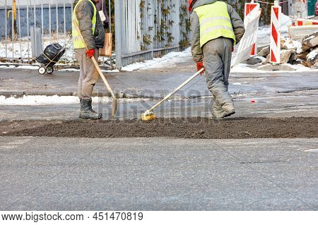 Road Workers Using A Shovel And Brush Patch Up The Road Surface On The Roadway And Cover It With Fin