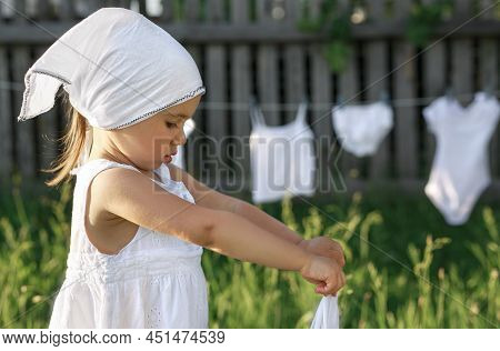 Profile Of A Girl In A White Scarf Washing Clothes. A Child Squeezes Wet Underwear. Mom's Little Hel