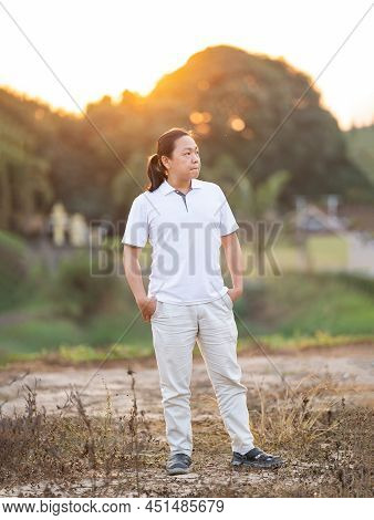 Asian Man Long Hair Stands And Relax On The Dry Field In Golden Twilight Time.