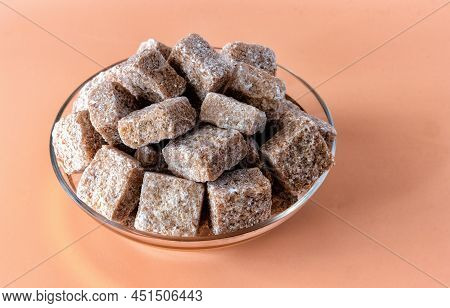 A Bunch Of Brown Sugar Cubes In A Glass Jar Against A Pink Background, Close Up View