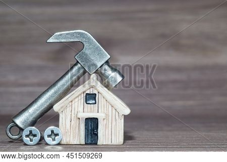 Small Steel Hammer And Screws By A Miniature House Model Against A Wooden Background. Home Repair Co