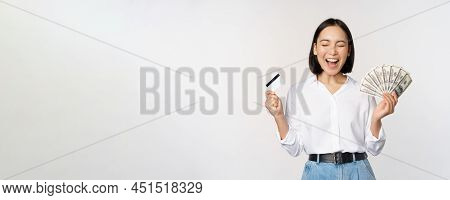 Finance And Money Concept. Happy Young Asian Woman Dancing With Cash And Credit Card, Smiling Please
