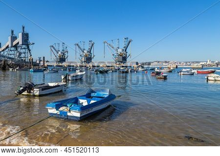Trafaria; Portugal - March 01; 2022: Deep water terminal and silo for grain, derived products and oleaginous products in Trafaria, Portugal with fishing boats near the beach