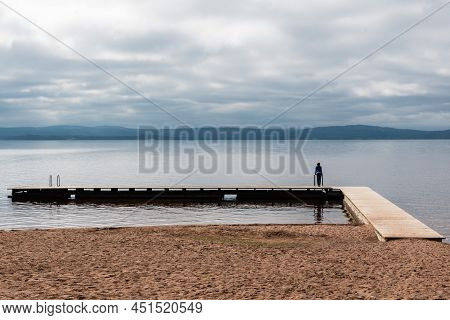 Woman Standing On A Rectanguar Shaped Pier At The Ljusnan River, Segersta, Halsingland, Sweden
