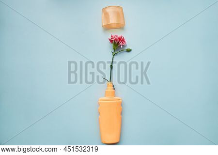 Skin Care Brightening Cosmetic Bottle Mock Up. Orange Beauty Product On Blue Background With Flower 