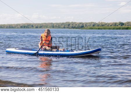 Little Blonde Girl Puddle Boarding On Lovely Lake Rowing With Oar In Hands Looking At Rippled Water 