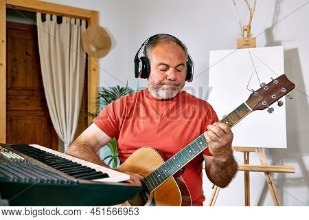 Pensive Mature Man Wearing Headphones Playing Acustic Guitar At Home. Music Hobby. Creative Leisure.