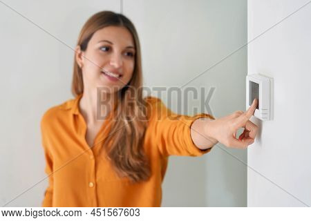 Lowering The Temperature For Energy Saving. Young Woman Adjusting Digital Central Heating Thermostat