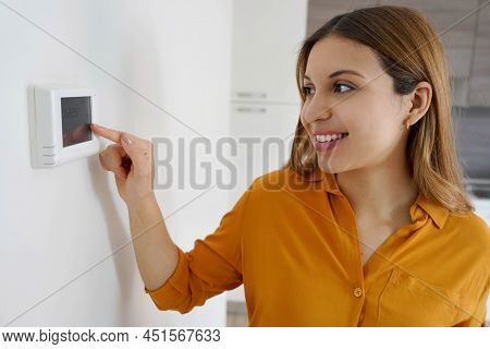 Portrait Of Smiling Woman Lowers The Temperature On Digital Thermostat At Home. Energy Saving, Effic