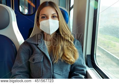 Young Woman Wearing Protective Face Mask Travels On Train Looking At Camera