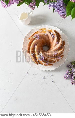 Classic Vanilla Bundt Cake With Sugar Glaze And Lilac Flowers On White Background. Spring Compositio
