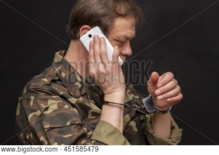 A Military Man In Handcuffs Makes A Phone Call On A Dark Background, Selective Focus. Concept: Priso