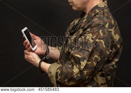 A Military Man In Handcuffs Makes A Phone Call On A Dark Background, Selective Focus. Concept: Priso