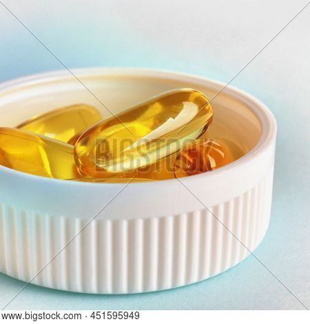 Fish Oil. Yellow Softgels Or Capsules Are In Bottle Cap. Blue And White Surface. Vitamins And Health