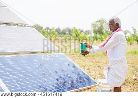 Indain Village Farmer Cleaning With Water On Solar Panels At Farmland - Concept Of Renewable Energy,