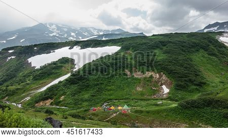 Bright Tourist Tents Stand In The Valley. The Paths Are Trodden In The Grass. Snowmelt On The Mounta