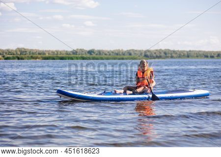Female Child Sup Boarding On Her Own On Calm Lake With Oar In Hands Looking At Water Ripples In Vest